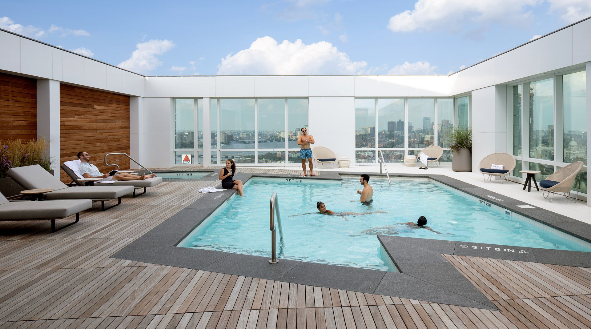 A rooftop pool with lounge chairs and a view of the city of Boston.