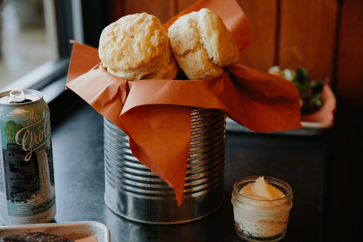 A tin of fresh baked biscuits served with a ramekin of whipped butter.