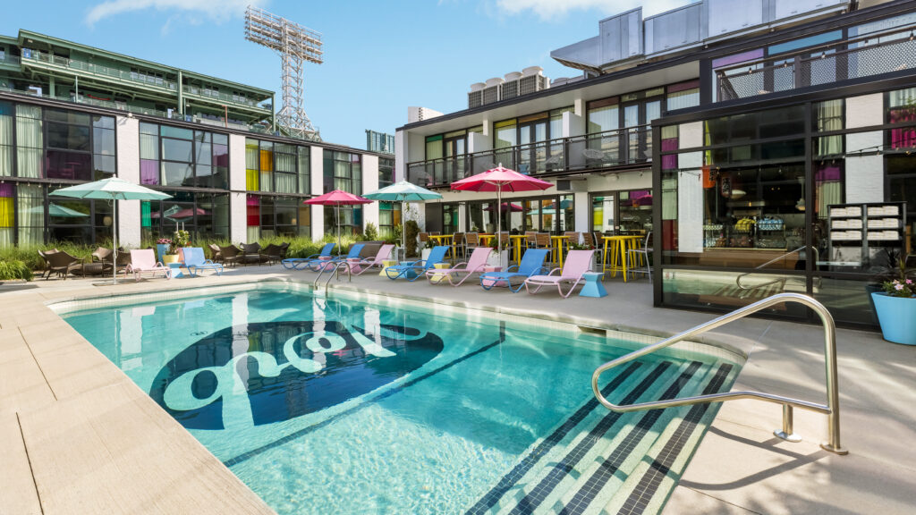 A pool with pastel-colored lounge chairs and umbrellas in front of the Verb Hotel in Fenway.