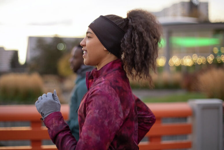 A young woman is dressed for cold weather as she runs outside in an urban environment.